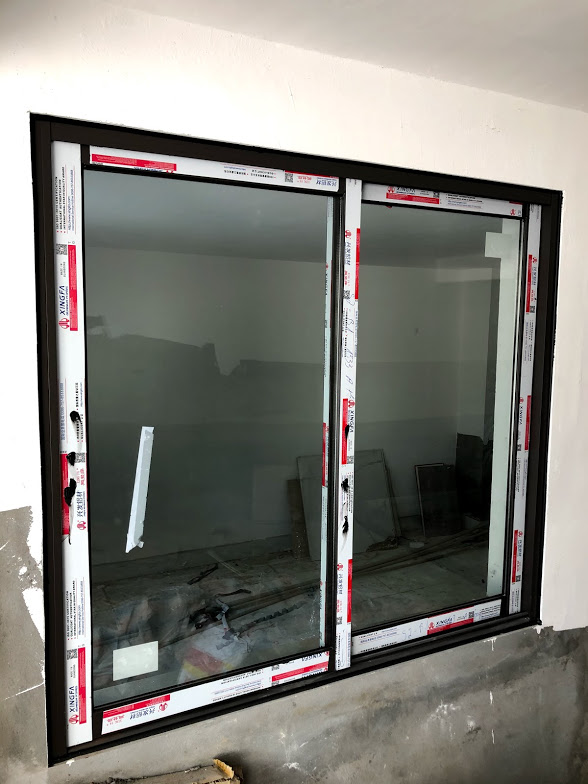 Cửa sổ kính trượt khung nhôm đang lắp đặt trong nhà, còn dán tem bảo vệ trên viền khung